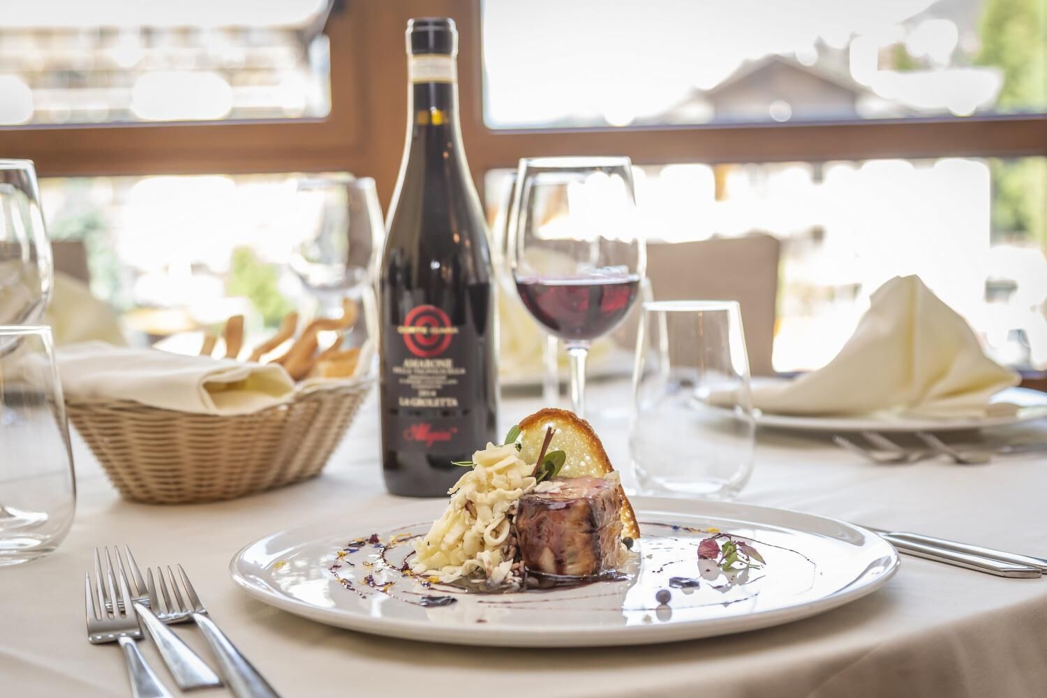 A dining table with a plate of food, a bottle of wine, and glasses.