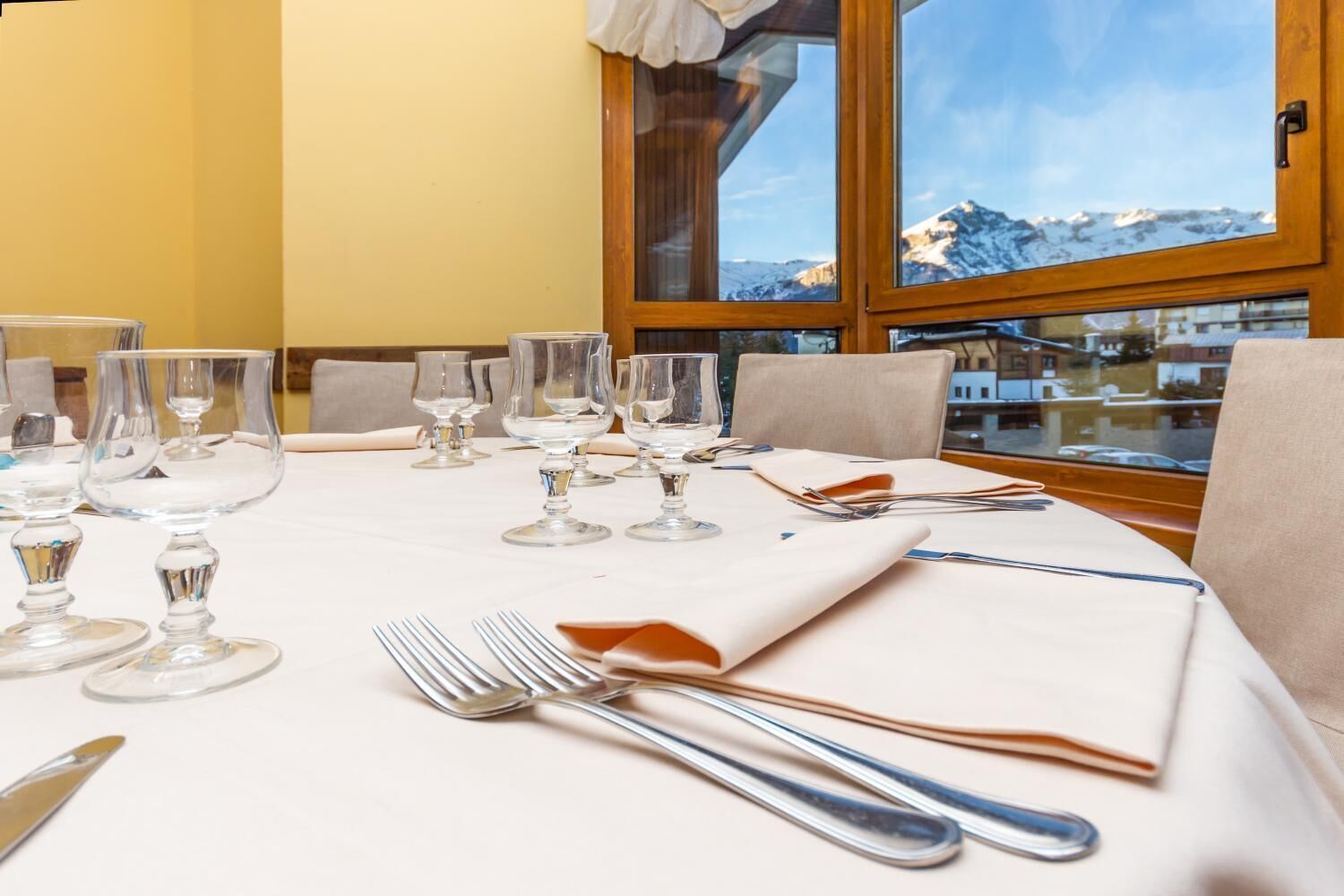 Un tavolo da pranzo apparecchiato con bicchieri da vino, forchette e coltelli, con vista sulle montagne attraverso una finestra.