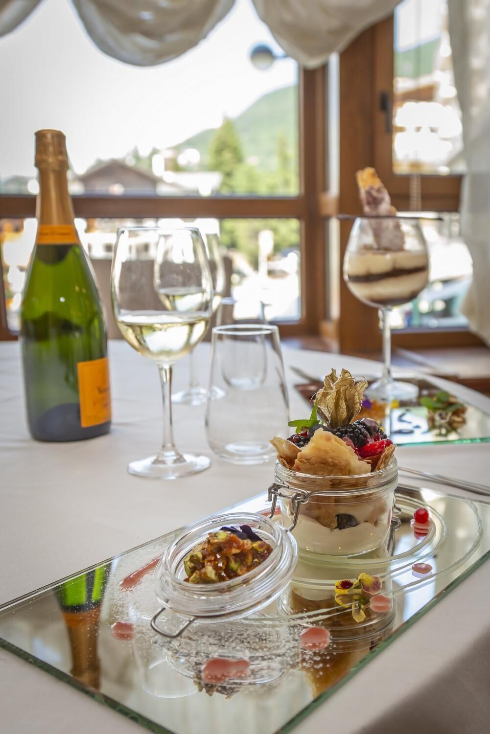 A table with a bottle of wine, empty wine glasses, and a dessert with berries and a chocolate piece on a glass tray.