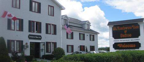 A two-story building with a sign for St. Andrews Inn & Suites, featuring a welcome sign, an American flag, and a sign indicating private waterfront balconies and an indoor heated pool.