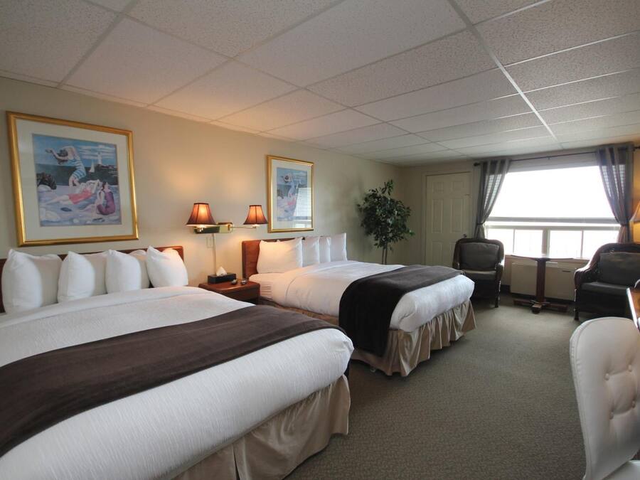A hotel room with two beds, a desk, a chair, and two lamps.