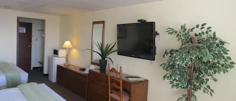 Habitación de hotel con cama, escritorio y silla, televisor, espejo y planta en maceta.