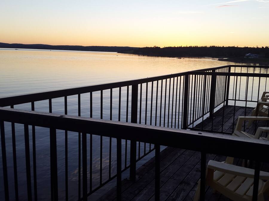 Une terrasse en bois avec une rambarde, donnant sur une étendue d’eau calme au coucher du soleil.
