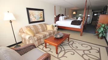 A hotel room with a four-poster bed, a sofa, a coffee table, a lamp, a painting, and a potted plant.