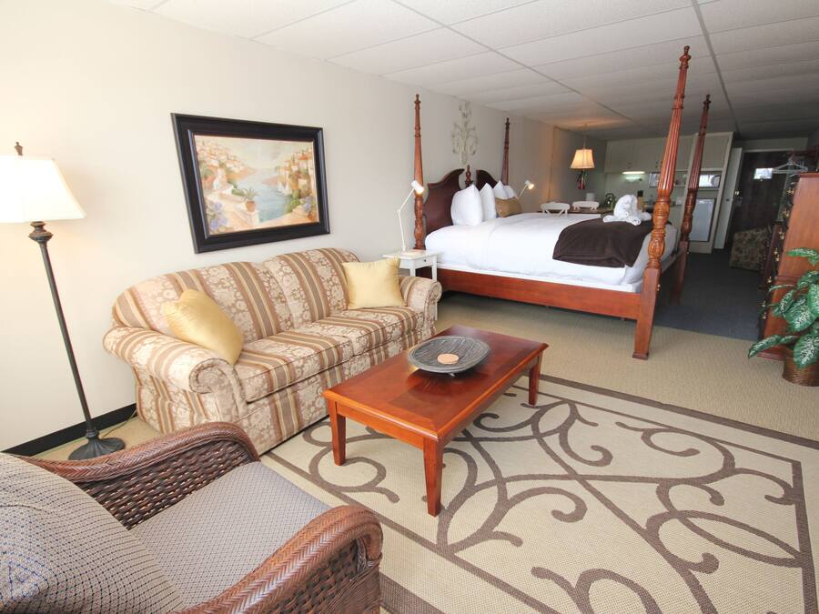 A hotel room with a four-poster bed, a sofa, a coffee table, a lamp, a painting, and a potted plant.