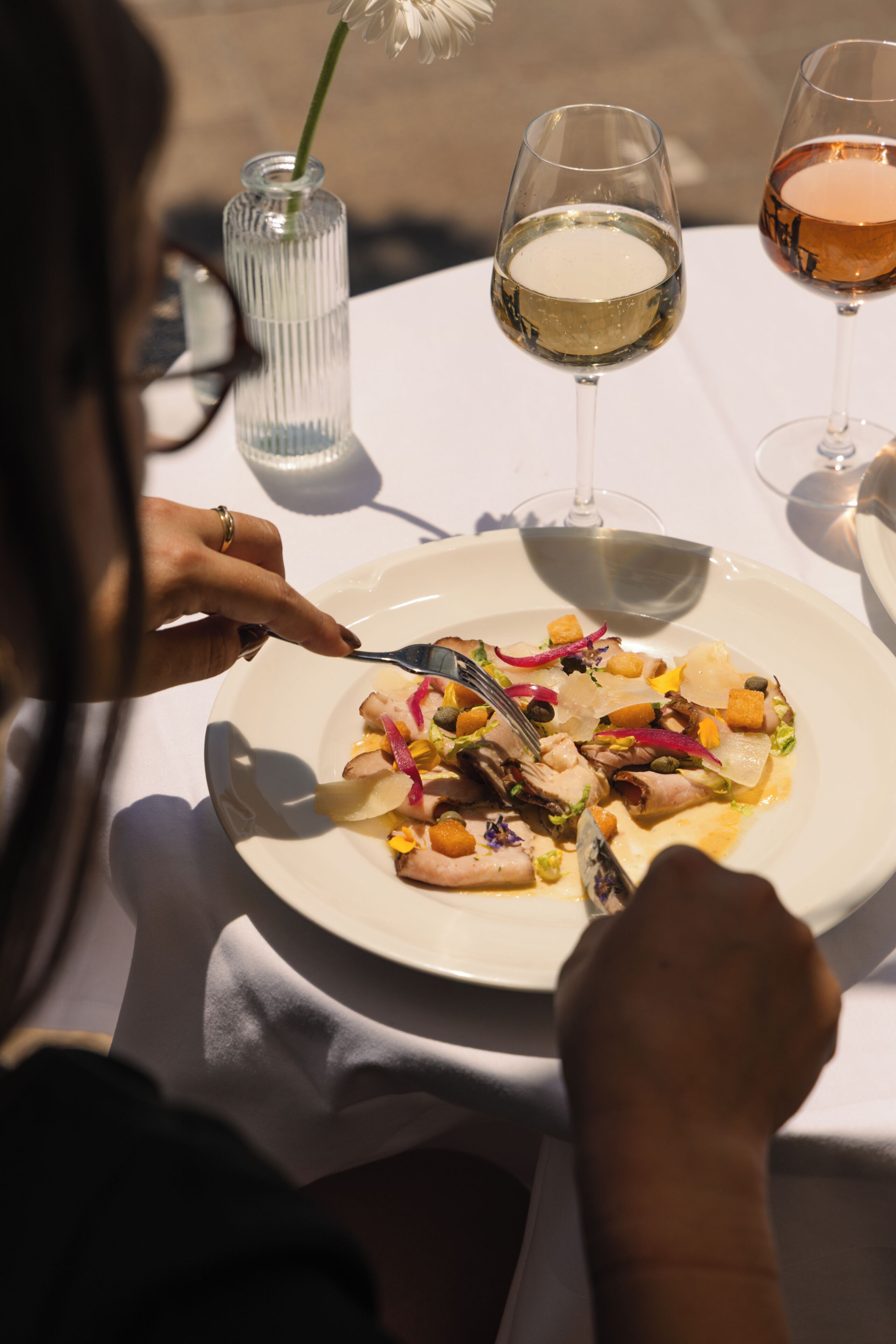 Una mesa de comedor con un plato de comida, una copa de vino blanco y una copa de vino rosado.