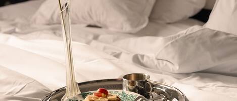 A neatly made bed with white linens, a tray with a plate of pancakes and a small cup, and a tall vase with a single green leaf.