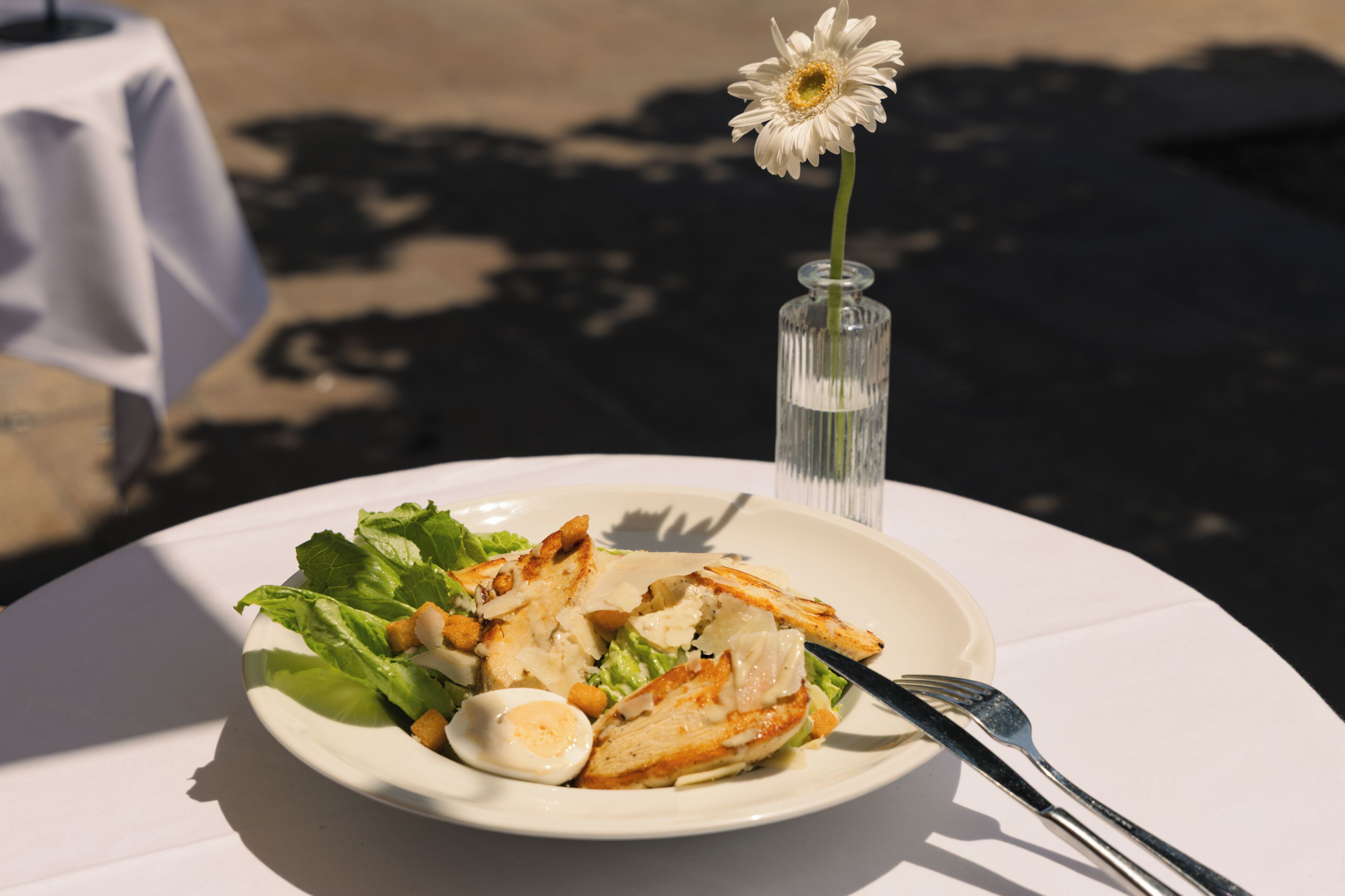 Un plato de comida con un tenedor y una jarra de vidrio con una sola flor.