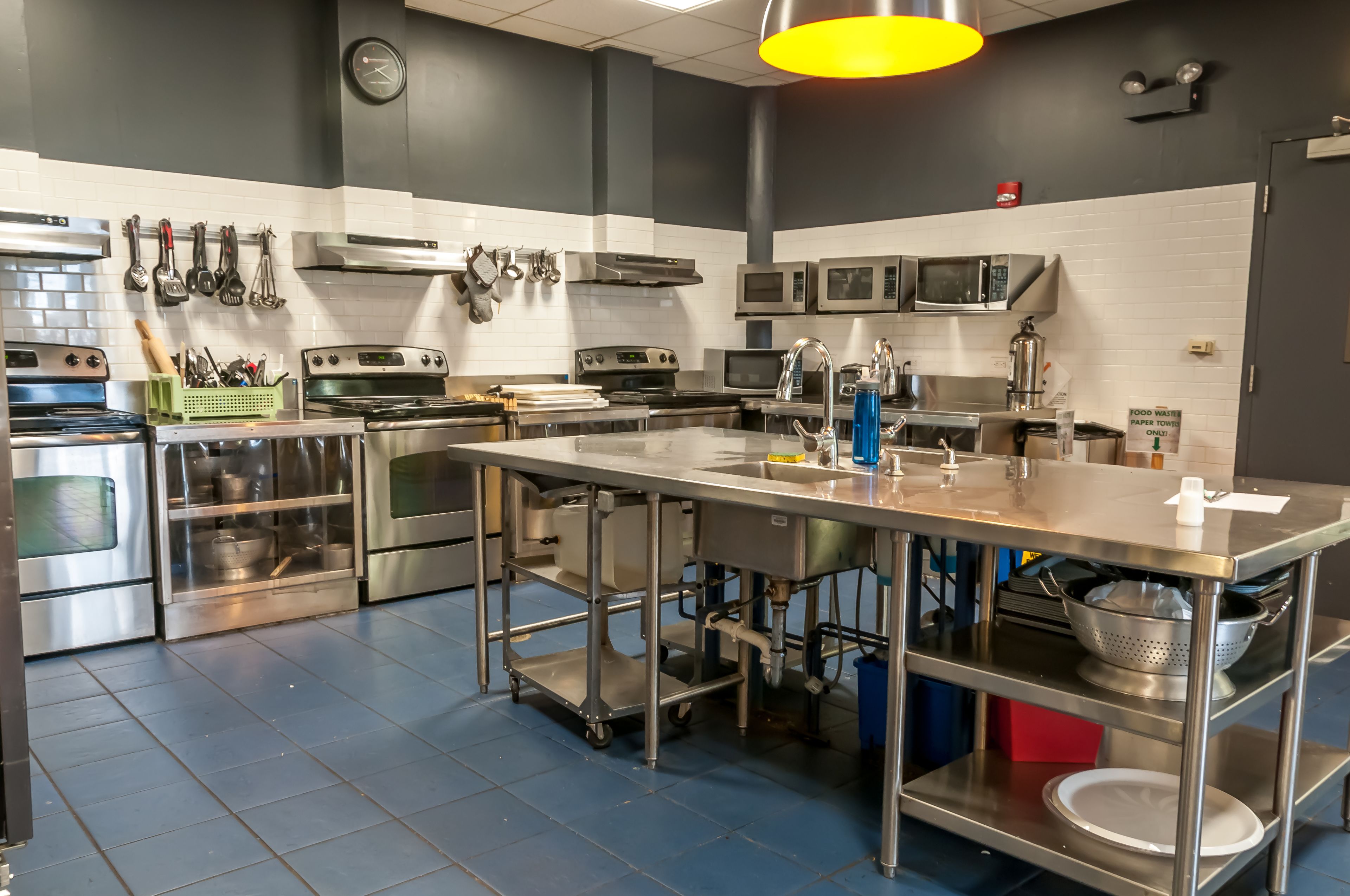 A modern kitchen with stainless steel appliances, a central island, and a variety of utensils hanging on the wall.