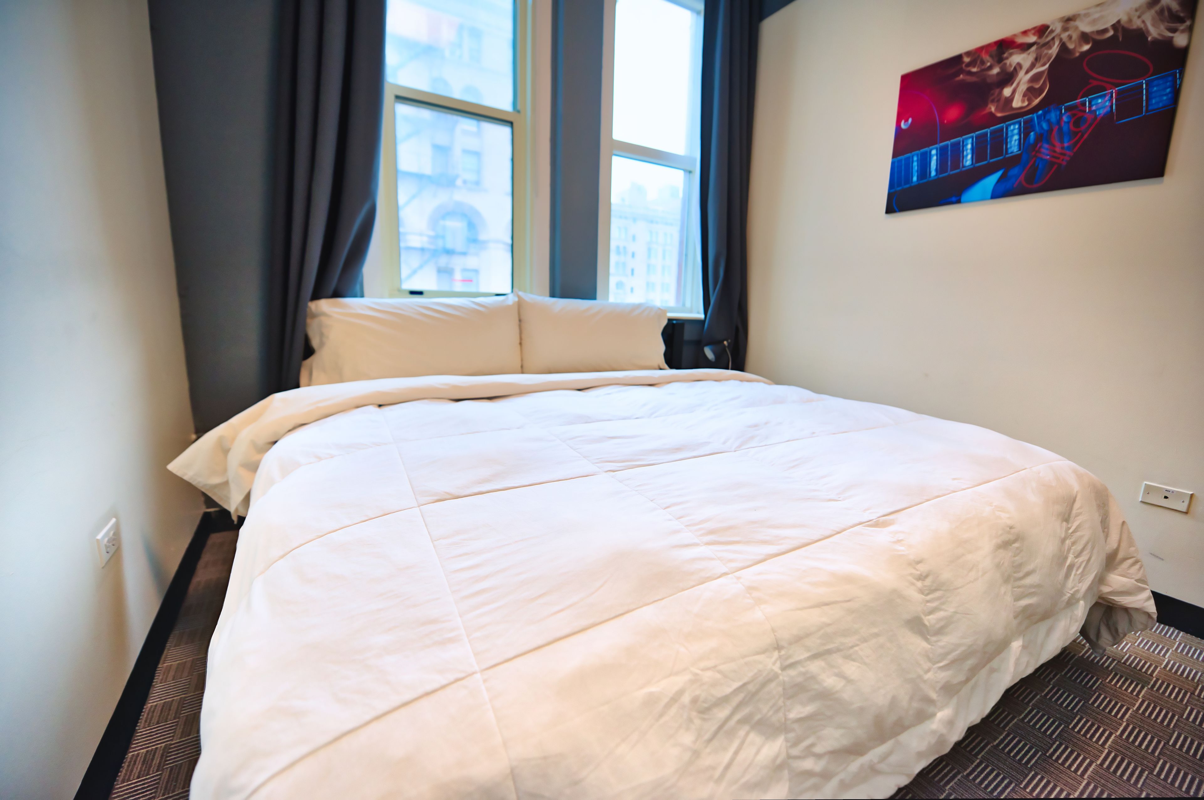 Une chambre d’hôtel avec un grand lit, une fenêtre avec des rideaux et un tableau au mur.