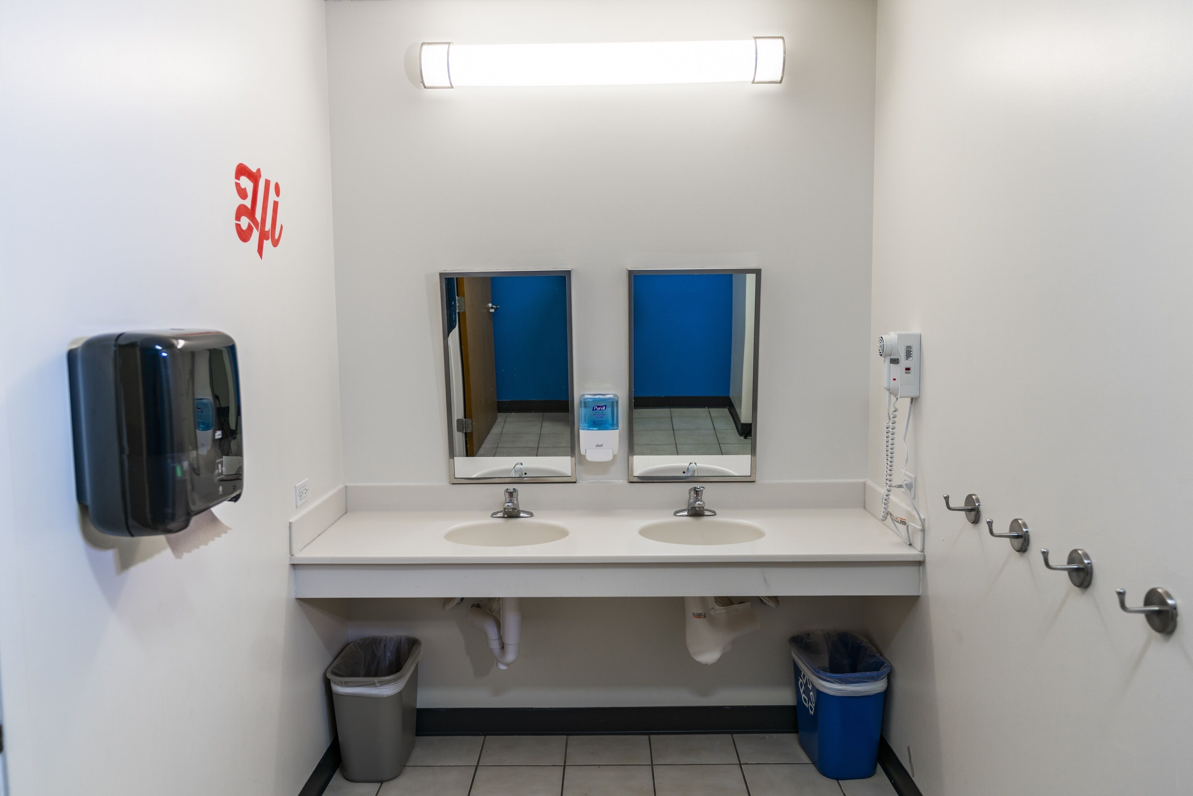 A public restroom with two sinks, mirrors, a soap dispenser, a trash bin, and a hand dryer.