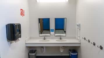 A public restroom with two sinks, mirrors, a soap dispenser, a trash bin, and a hand dryer.