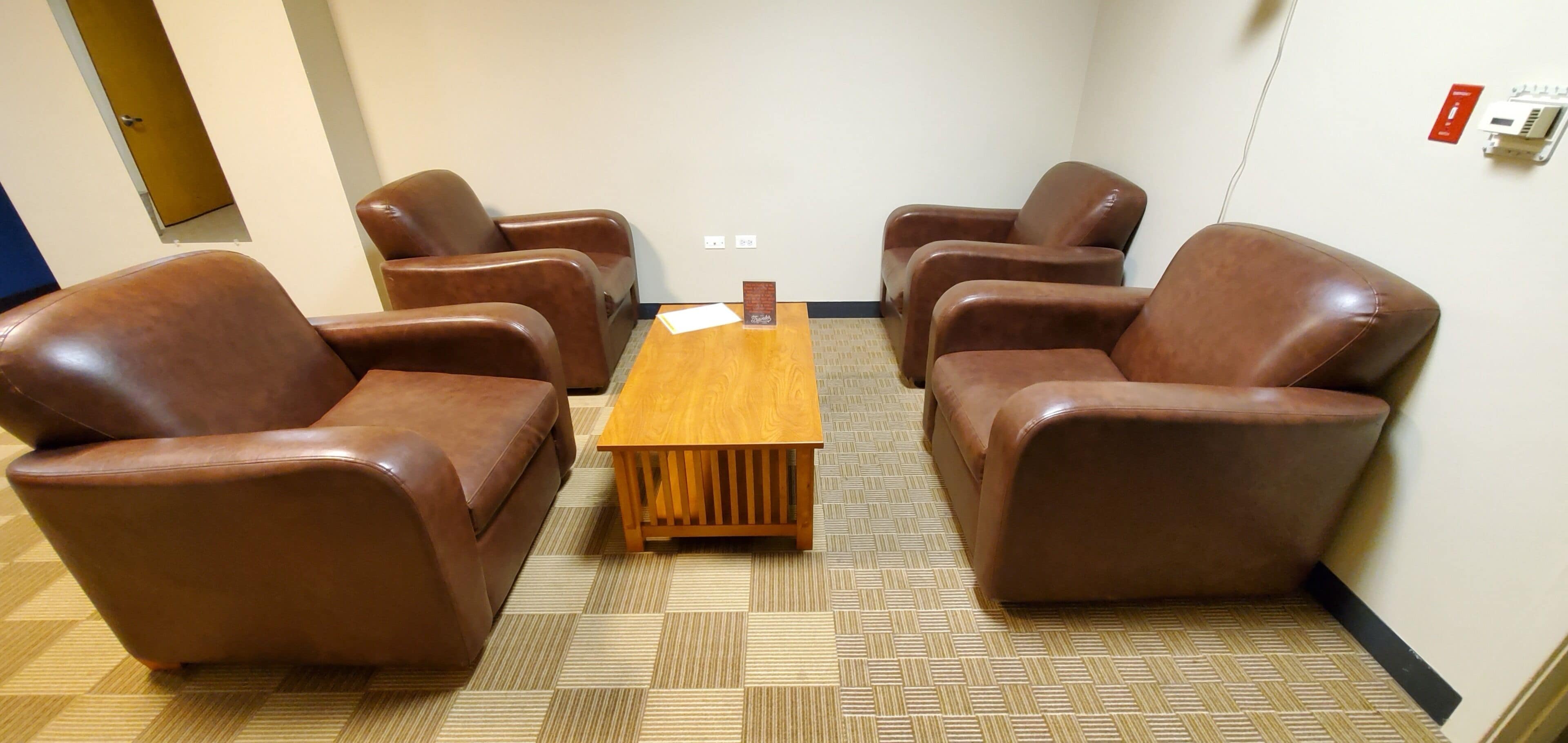 Een kamer met vier bruine lederen stoelen en een houten tafel.