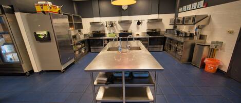 A commercial kitchen with stainless steel appliances, a central island, and a blue tiled floor.
