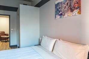 Una habitación de hotel moderna con una cama, una puerta que da a una sala de estar y un cuadro de paisaje urbano en la pared.