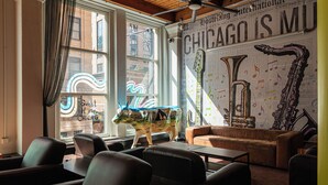 A cozy lounge with leather seating, a large window with curtains, and a wall decorated with musical instruments and a neon sign. - HI Chicago Hostel (Chicago)