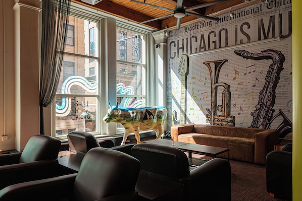 A cozy lounge with leather seating, a large window with curtains, and a wall decorated with musical instruments and a neon sign.