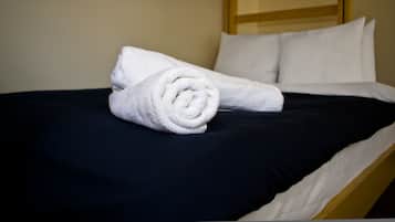 A neatly made bed with a rolled white towel and two white pillows on a dark blue bedspread.
