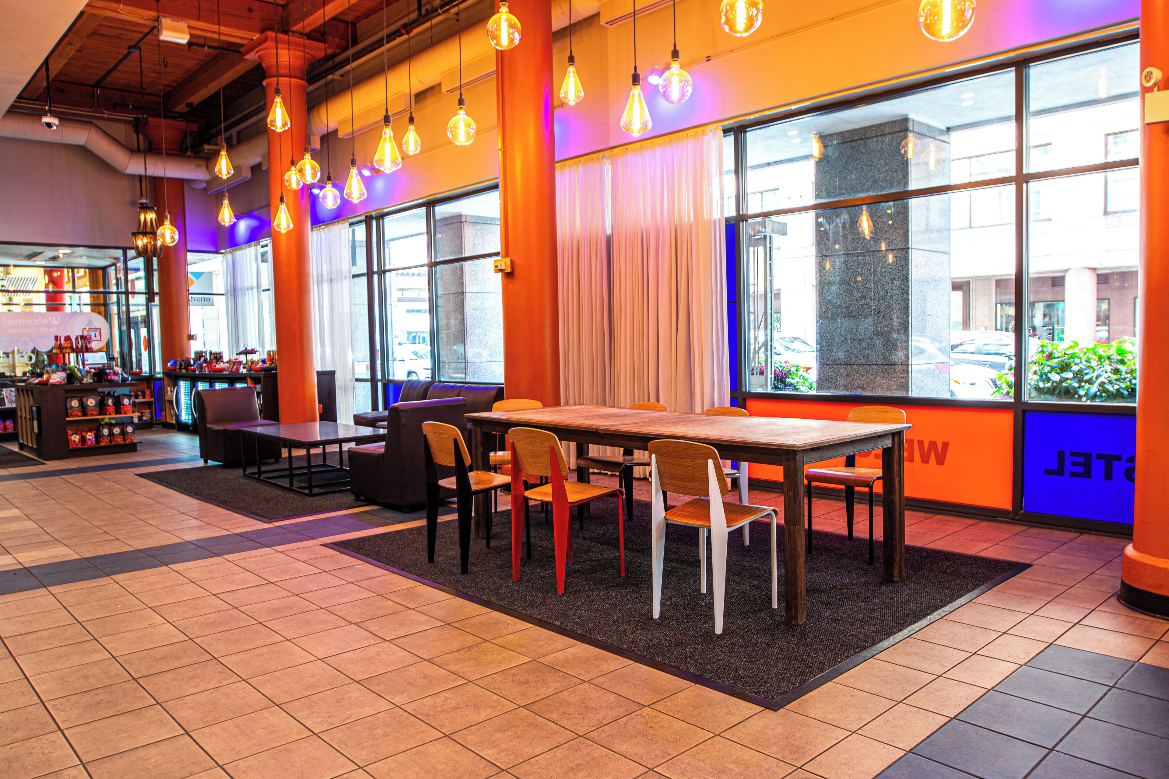 Un restaurant moderne avec une longue table et des chaises en bois, de grandes fenêtres avec des rideaux et des lampes suspendues.