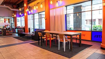 Un restaurant moderne avec une longue table et des chaises en bois, de grandes fenêtres avec des rideaux et des lampes suspendues.