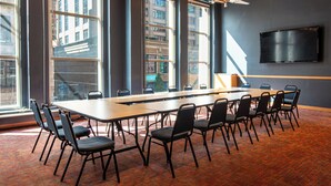 A conference room with a long table, chairs, large windows, a flat-screen TV, and a ceiling fan.