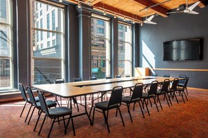 A conference room with a long table, chairs, large windows, a flat-screen TV, and a ceiling fan.