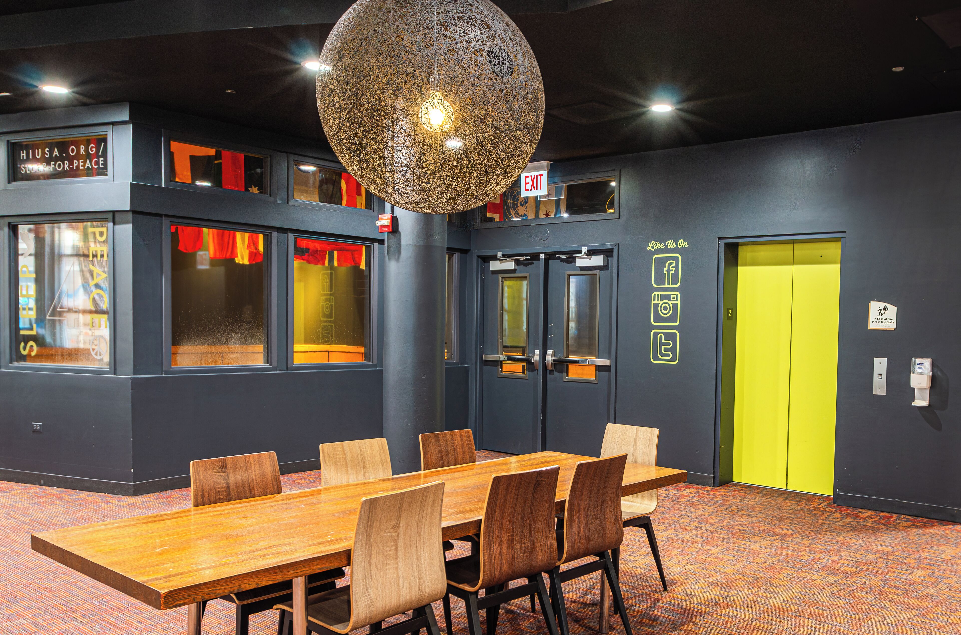 A conference room with a large wooden table and chairs, a spherical hanging light fixture, and a bright yellow door.