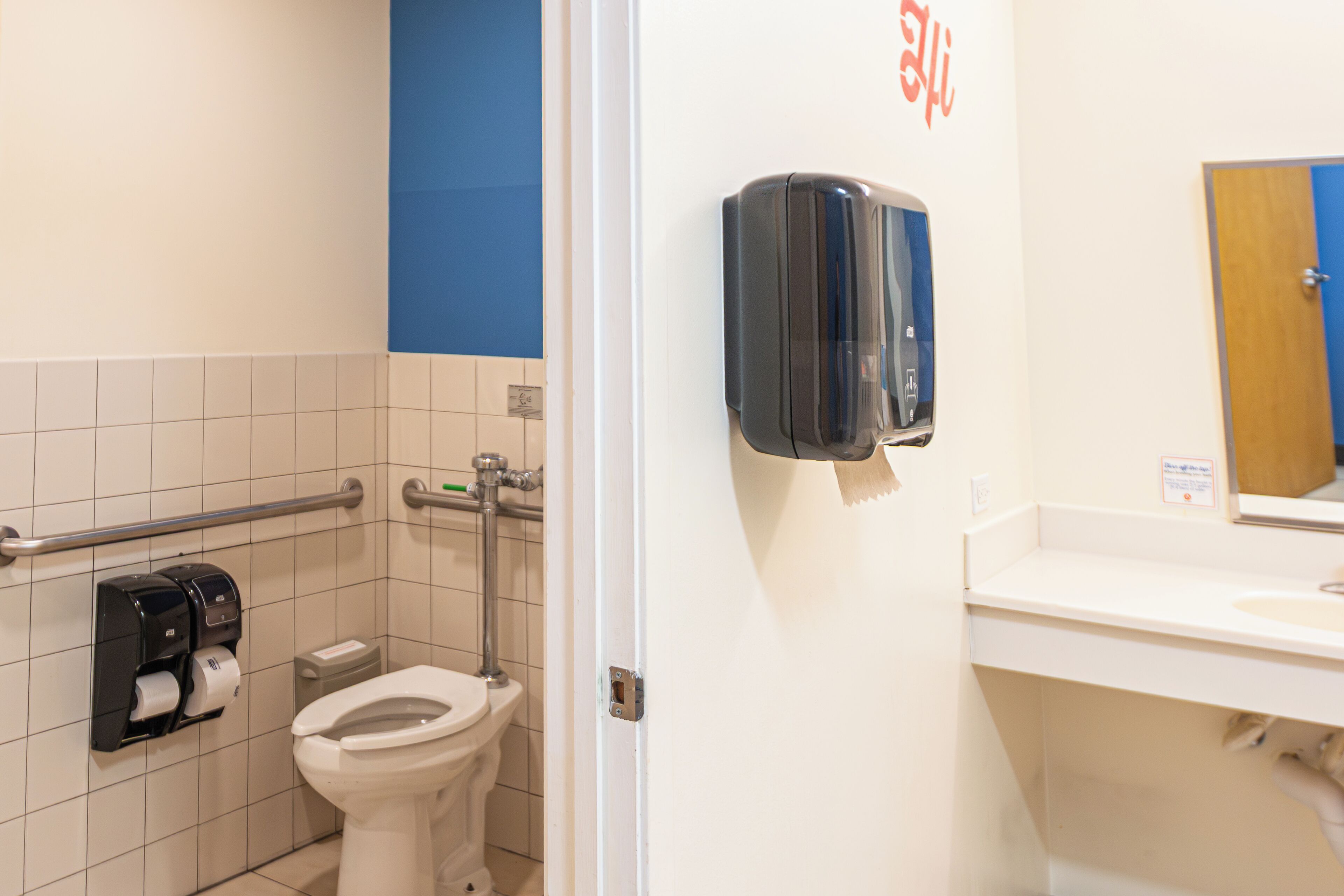 A bathroom with a toilet, hand dryer, and paper towel dispenser.