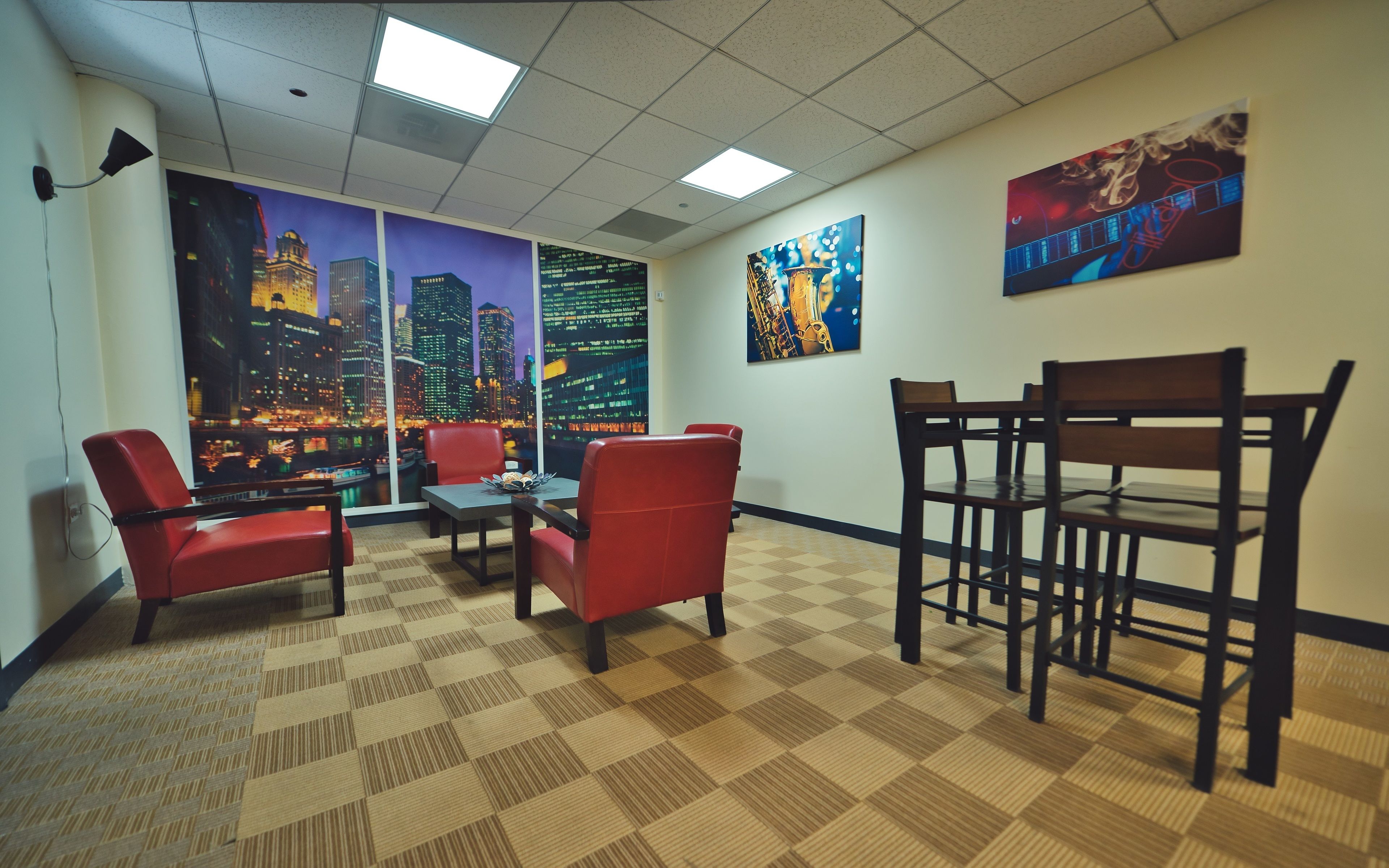 A conference room with a cityscape view, red chairs, a table, and two paintings on the walls.
