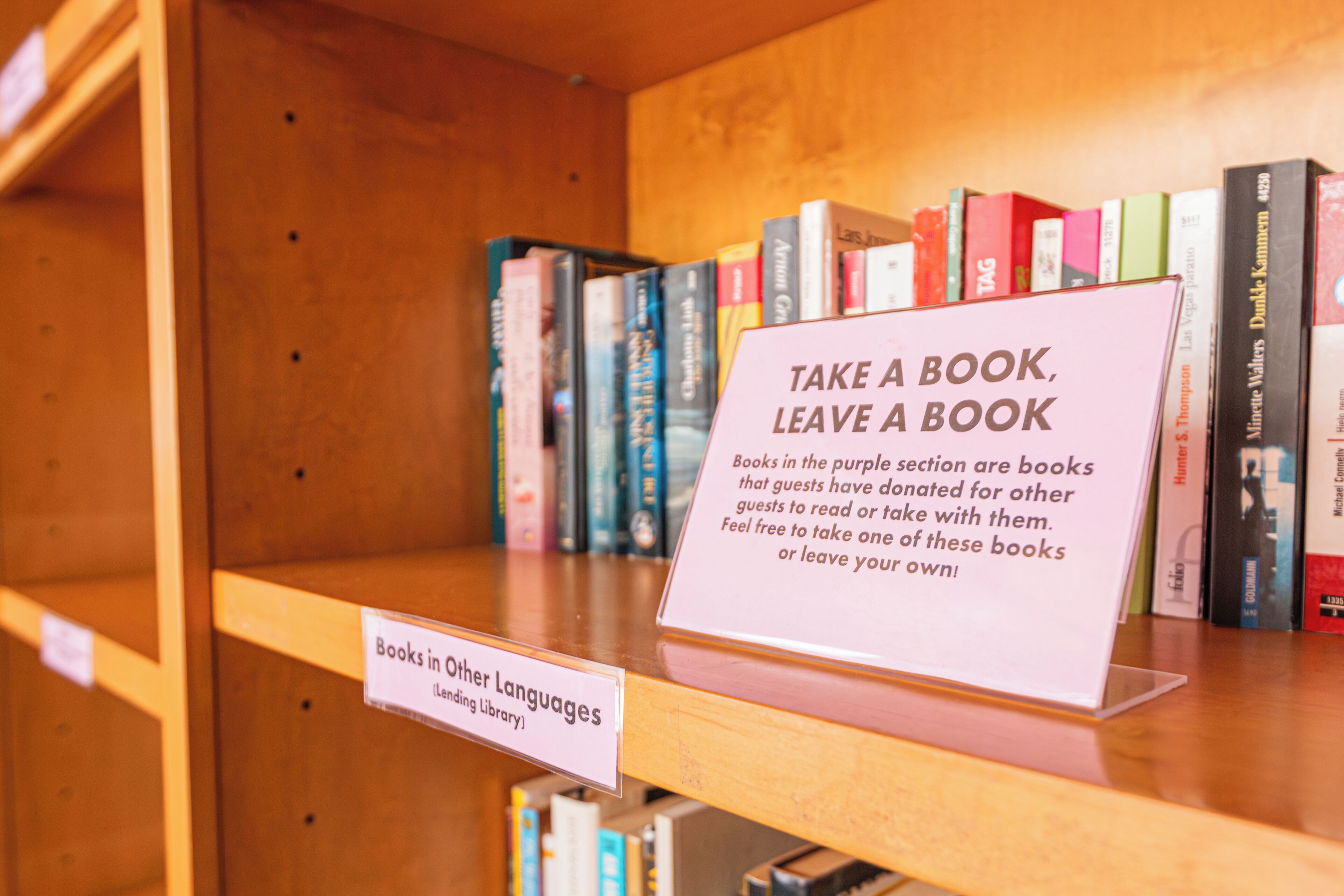 Uma estante com um letreiro que diz 'Pegue um livro, deixe um livro' e outro indicando 'Livros em outros idiomas'.