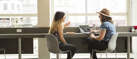 Two people seated at a table in a modern cafe with large windows and a view of buildings outside.