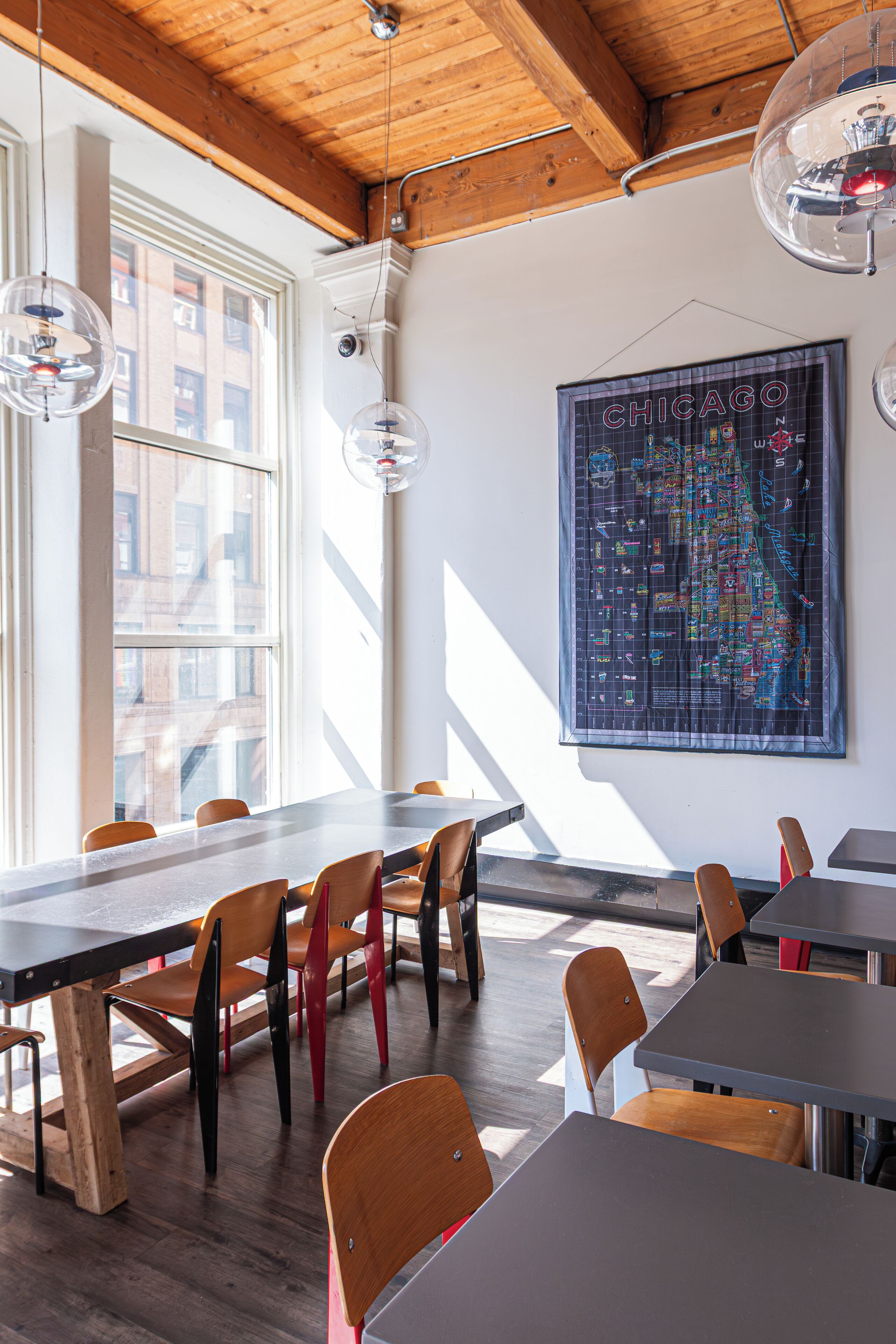 A dining area with wooden tables and chairs, a large map on the wall, and large windows allowing natural light.