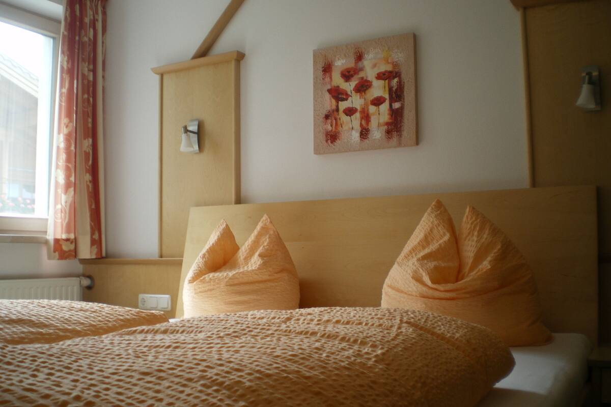 A hotel room with a bed, a painting on the wall, and a window with curtains.