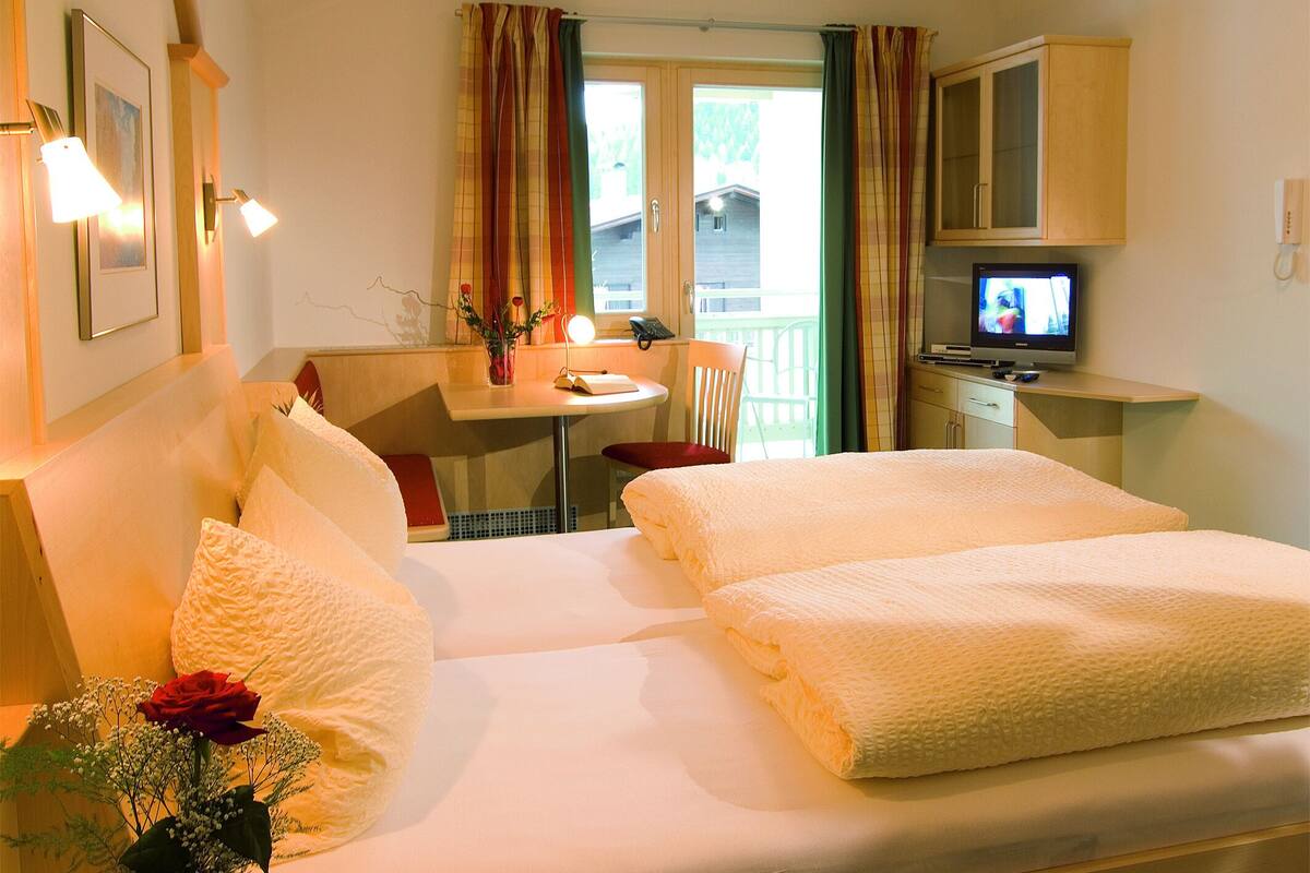 A hotel room with two beds, a desk with a chair, a television, and a window with curtains.