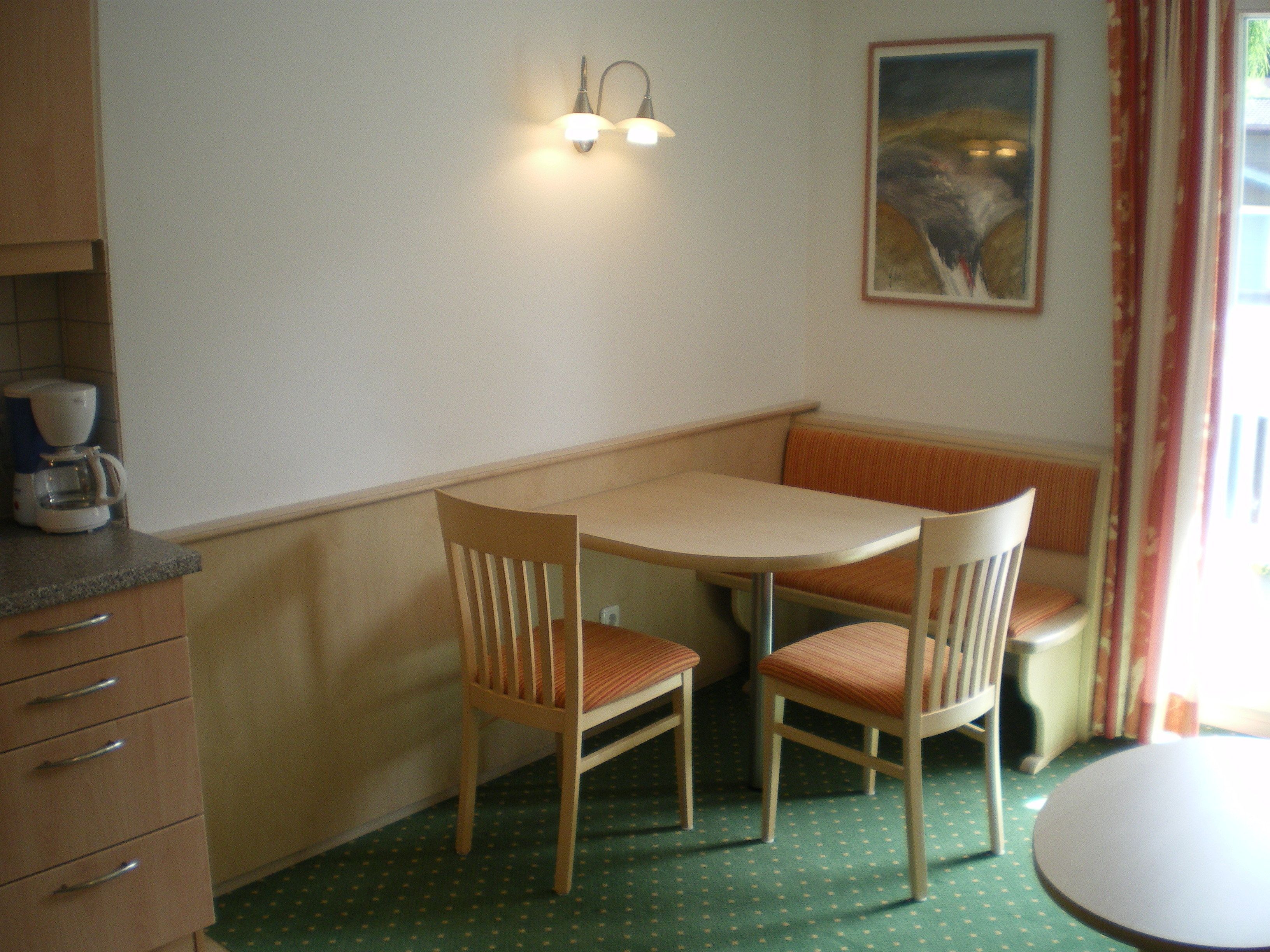 A small dining area with a table and two chairs, a coffee maker on the counter, and a painting on the wall.