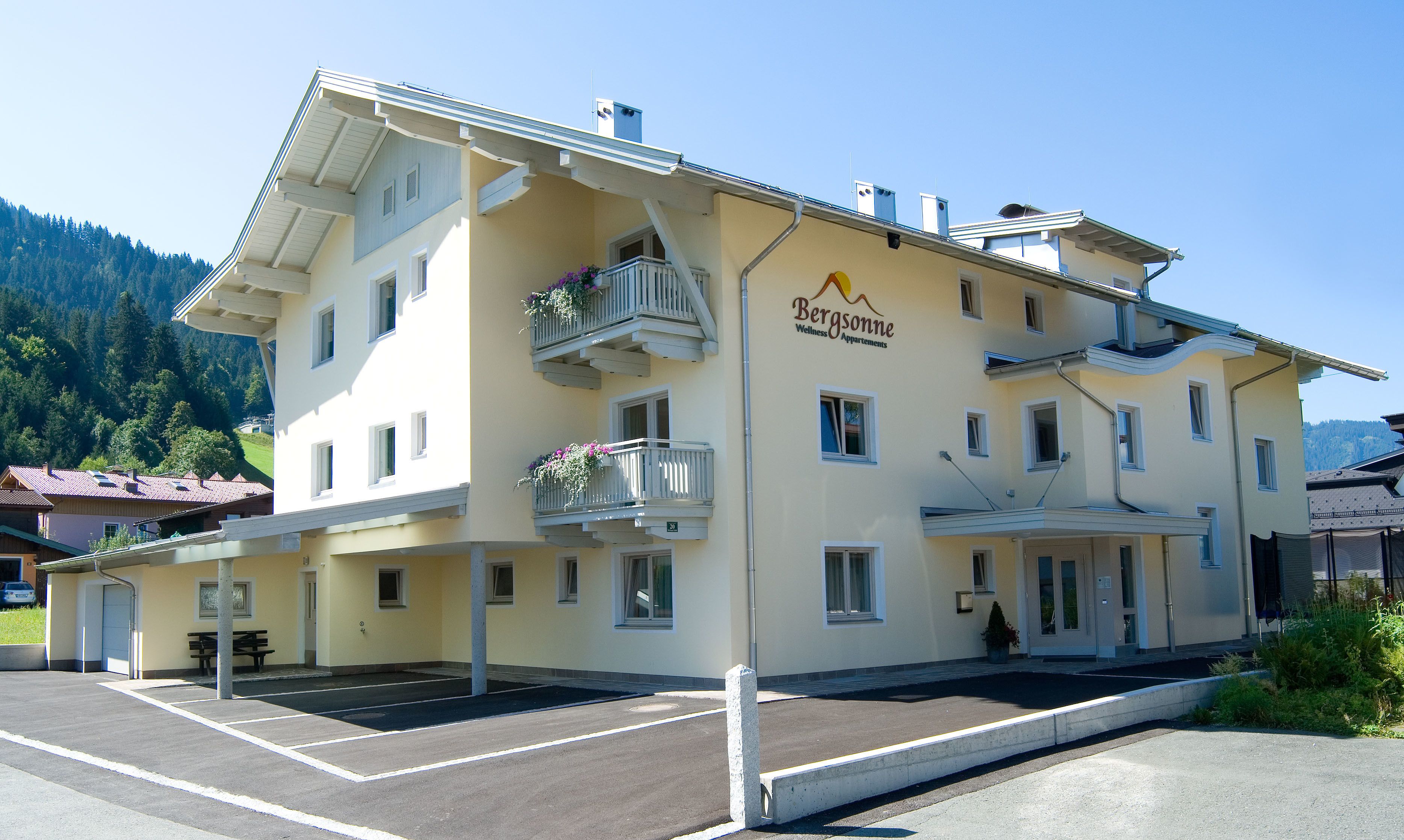 Um edifício com vários andares e varandas, com uma placa indicando "Bergsomme Wellness Apartments" e uma área de estacionamento em frente.