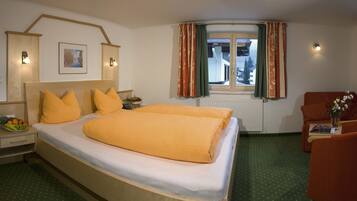 Una habitación de hotel con una cama grande, un escritorio, una silla, una ventana con cortinas y una lámpara fijada a la pared.