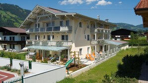A multi-story hotel with a balcony, outdoor seating area, and a children's play structure. - Appartements Bergsonne (Westendorf)