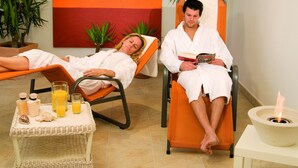 Two people in a spa-like setting with orange chairs, a small table with drinks and snacks, and a fire feature. - Appartements Bergsonne (Westendorf)