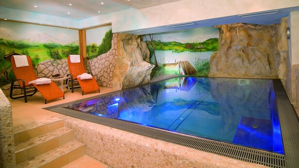 A spa area with a large indoor pool, stone walls, and relaxation chairs. - Appartements Bergsonne (Westendorf)