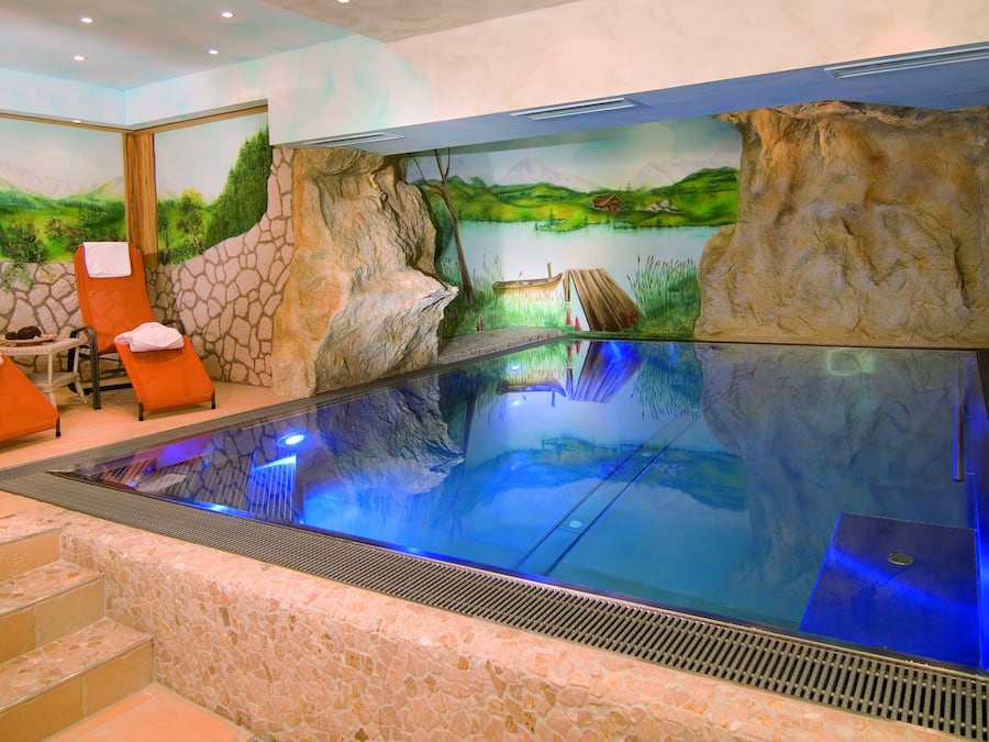 Un área de spa con una amplia piscina cubierta, paredes de piedra y sillones de relax.