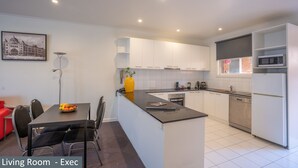 A modern kitchen with white cabinetry, a central island, and a dining area with a red chair.