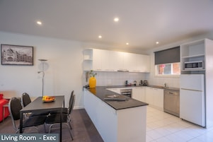 Una cocina moderna con armarios blancos, una isla central y un comedor con una silla roja.
