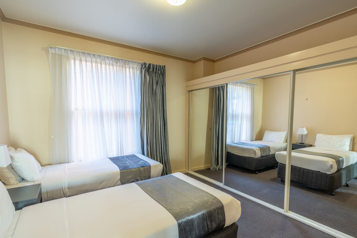 Habitación de hotel con dos camas, un espejo grande y vista a la ciudad.