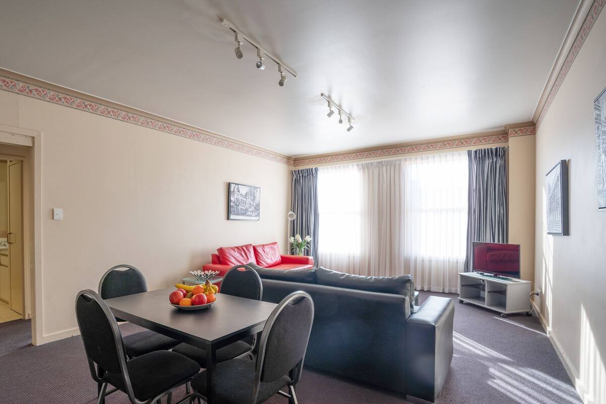 Una sala de estar moderna con comedor, sofá, televisión y ventana con cortinas.