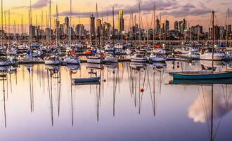 Un puerto deportivo con numerosas embarcaciones amarradas, rodeado por el perfil urbano de una ciudad con edificios modernos.