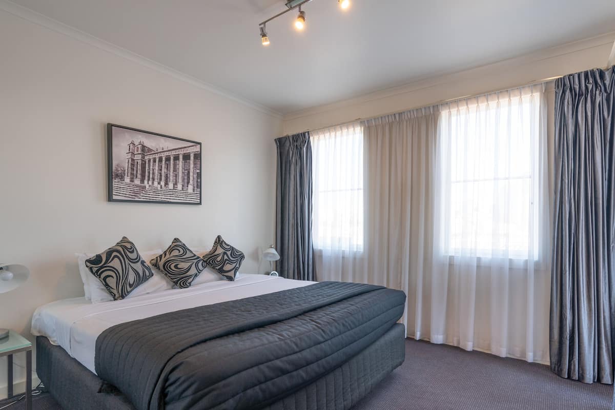 Una habitación de hotel con una cama grande, una mesita de noche, una lámpara y una ventana con cortinas.