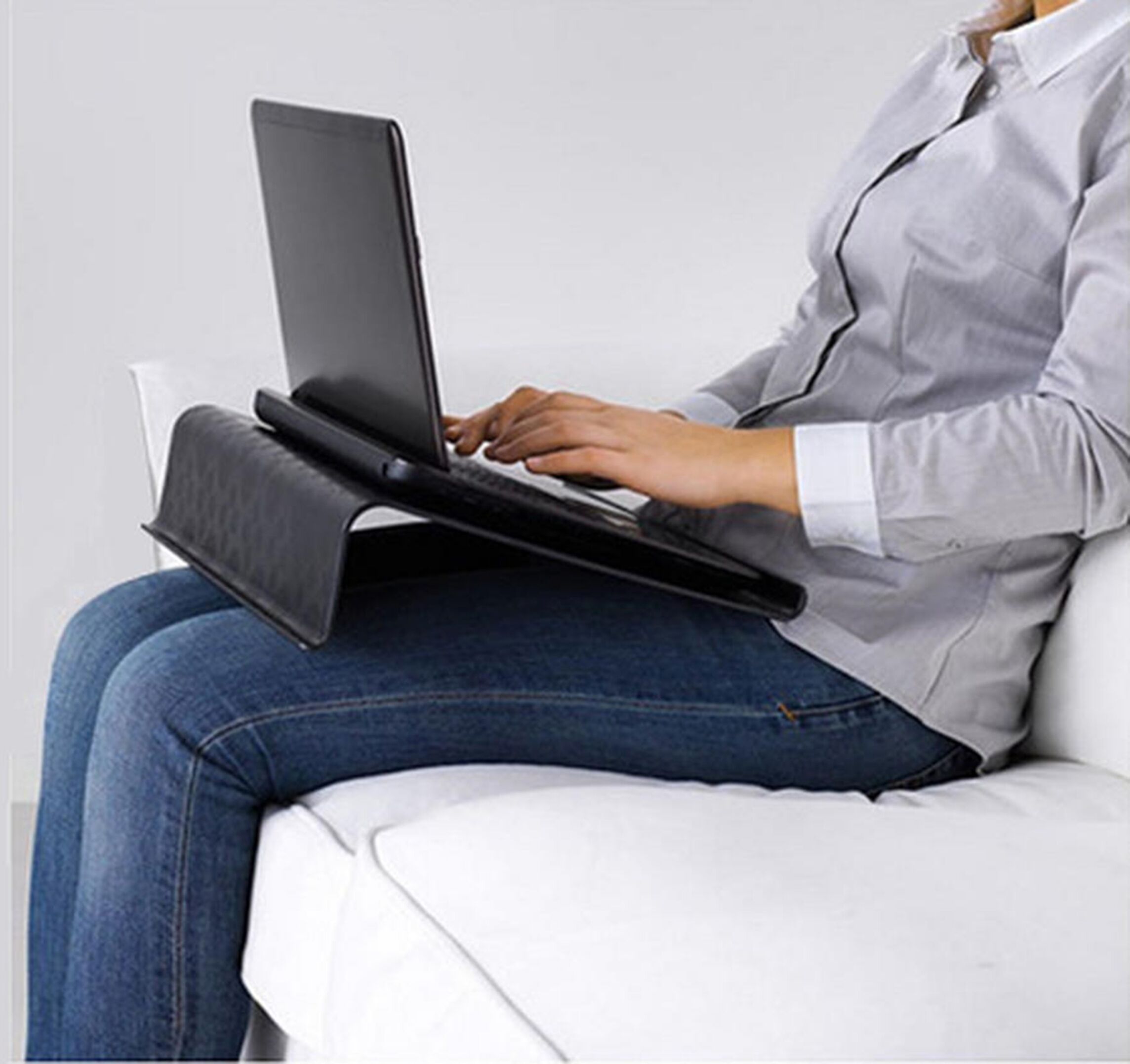Eine Person sitzt auf einem weißen Sofa und benutzt einen Laptop, der auf einem Laptopständer steht.