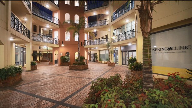 A multi-level atrium with a central courtyard, featuring a Spring Clinic sign, multiple balconies, and potted plants.