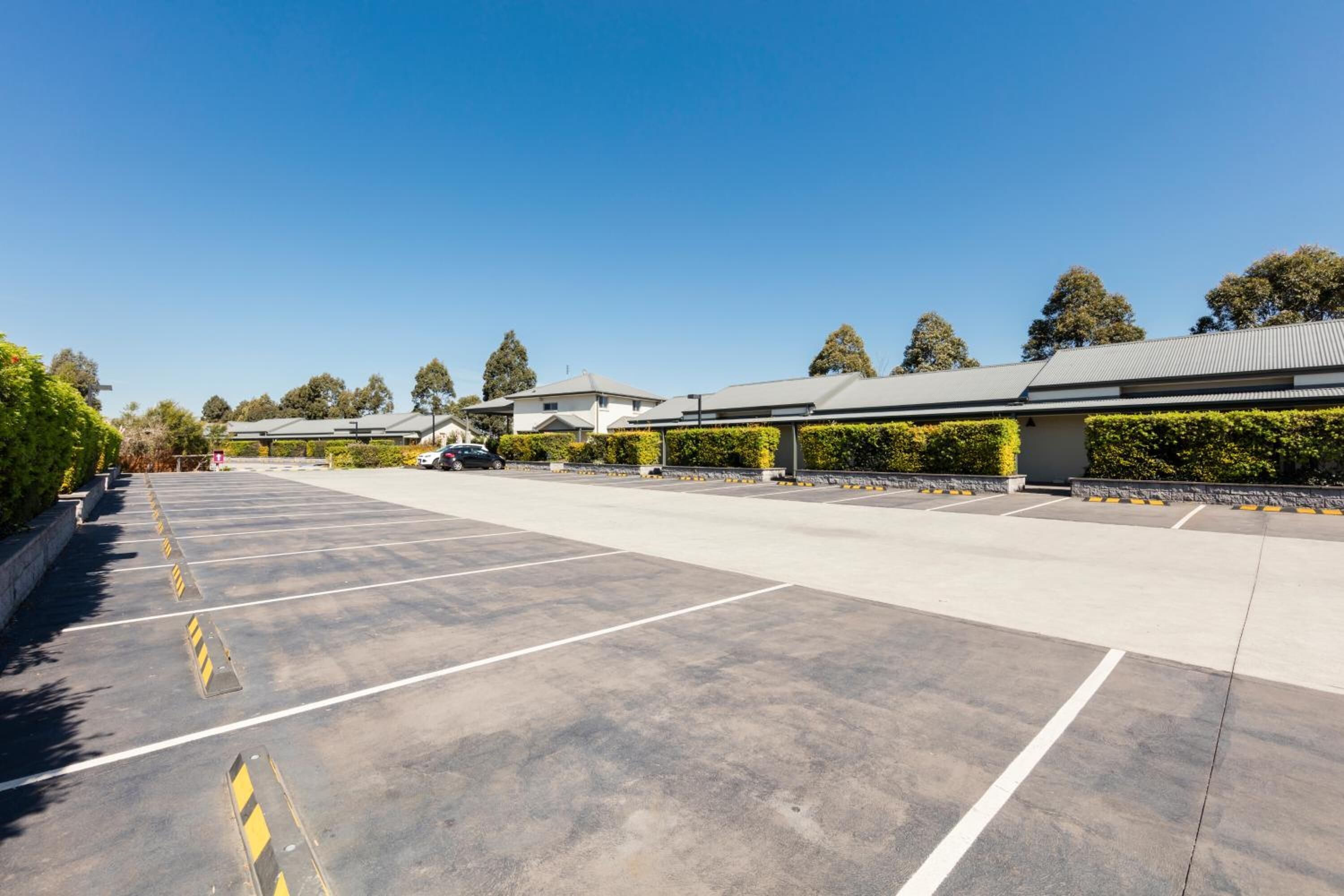 A parking lot with marked spaces and yellow bollards, surrounded by buildings and trees.